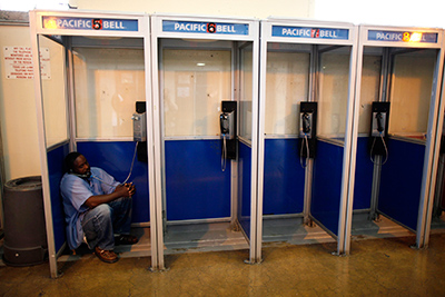 image of an incarcerated man at San Quentin prison crouching down in a phone booth on the phone